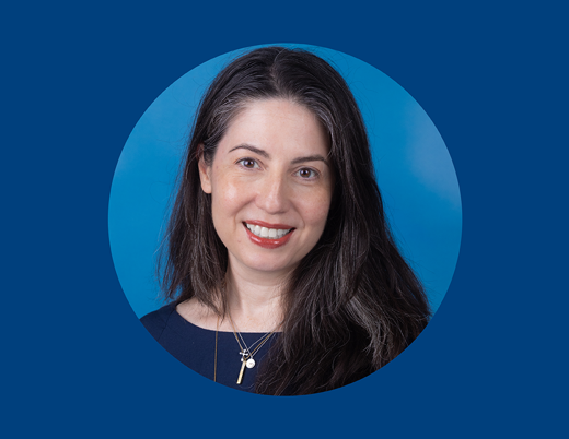 A woman with dark hair wearing multiple necklaces smiles in front of a blue background and in a circular frame.