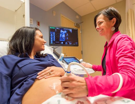 Doctor holds ultrasound wand on pregnant patients belly while seeing baby on the screen and smiling at each other.