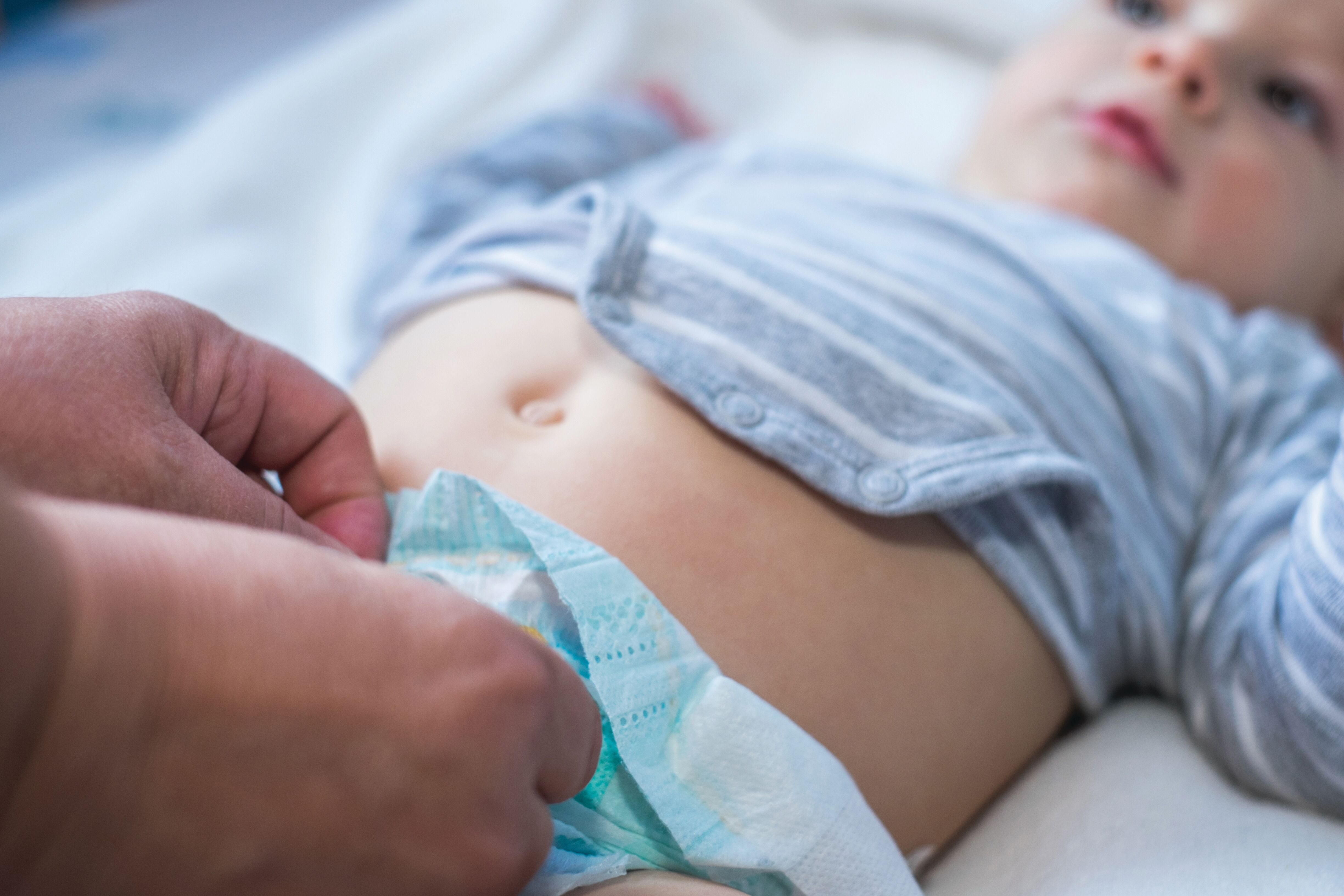 Close-up of a baby lying down while an adult fastens or adjusts the baby’s diaper.