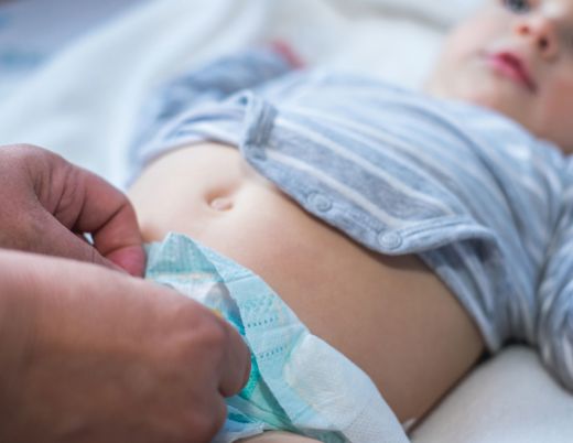Close-up of a baby lying down while an adult fastens or adjusts the baby’s diaper.