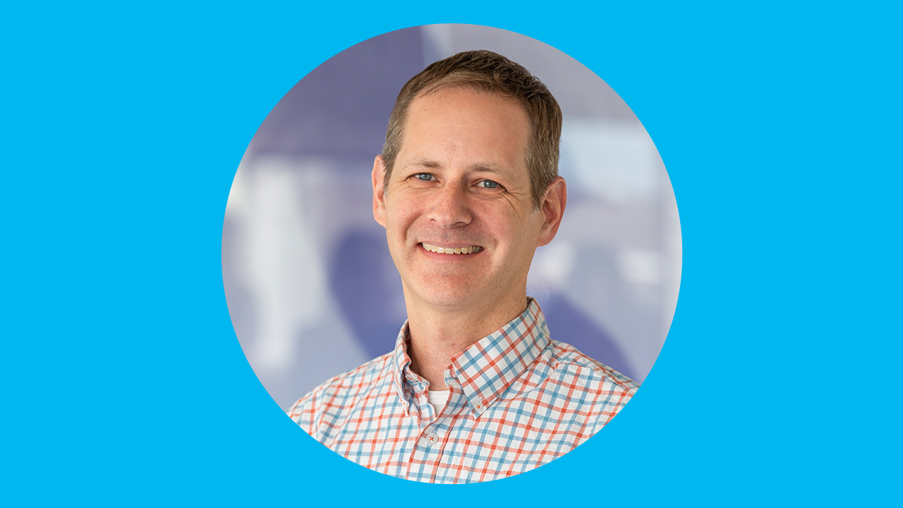 A doctor smiles for a headshot on a simple graphic. 