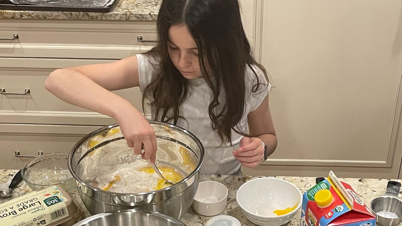 A 10-year-old girl with long brown hair makes batter for pancakes.
