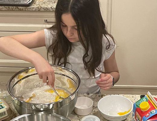 A 10-year-old girl with long brown hair makes batter for pancakes.