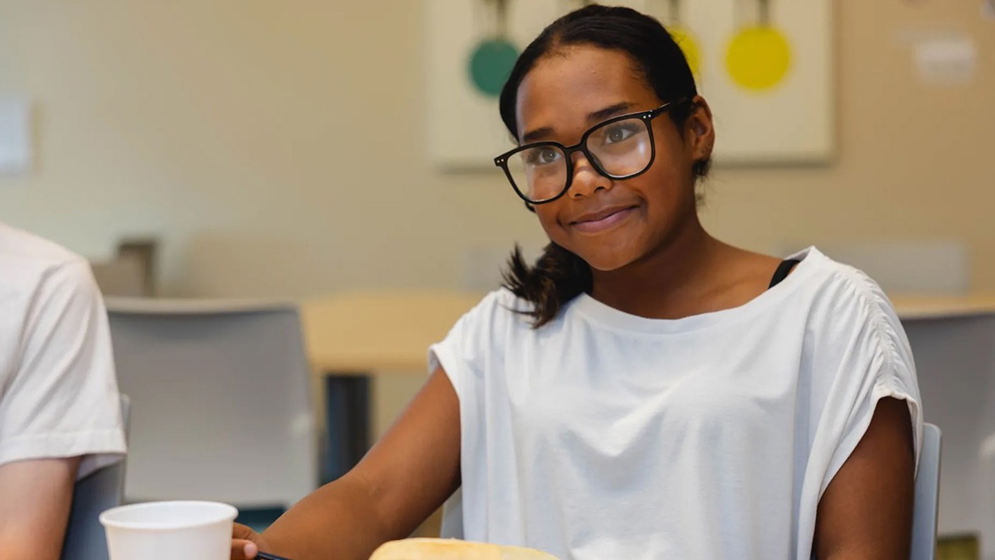 A child wearing a white t-shirt smiles while sitting at a desk.