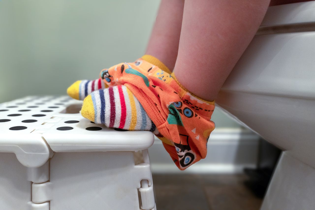 A child's feet in colorful socks resting on a stool while sitting on a toilet seat, showcasing an encouraging moment in potty training.