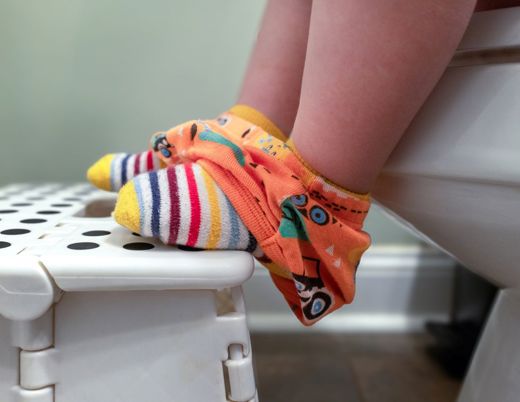 A child's feet in colorful socks resting on a stool while sitting on a toilet seat, showcasing an encouraging moment in potty training.