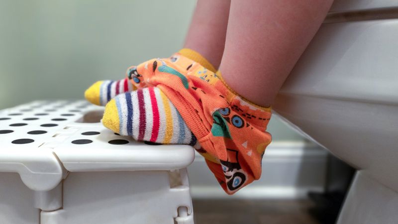 A child's feet in colorful socks resting on a stool while sitting on a toilet seat, showcasing an encouraging moment in potty training.