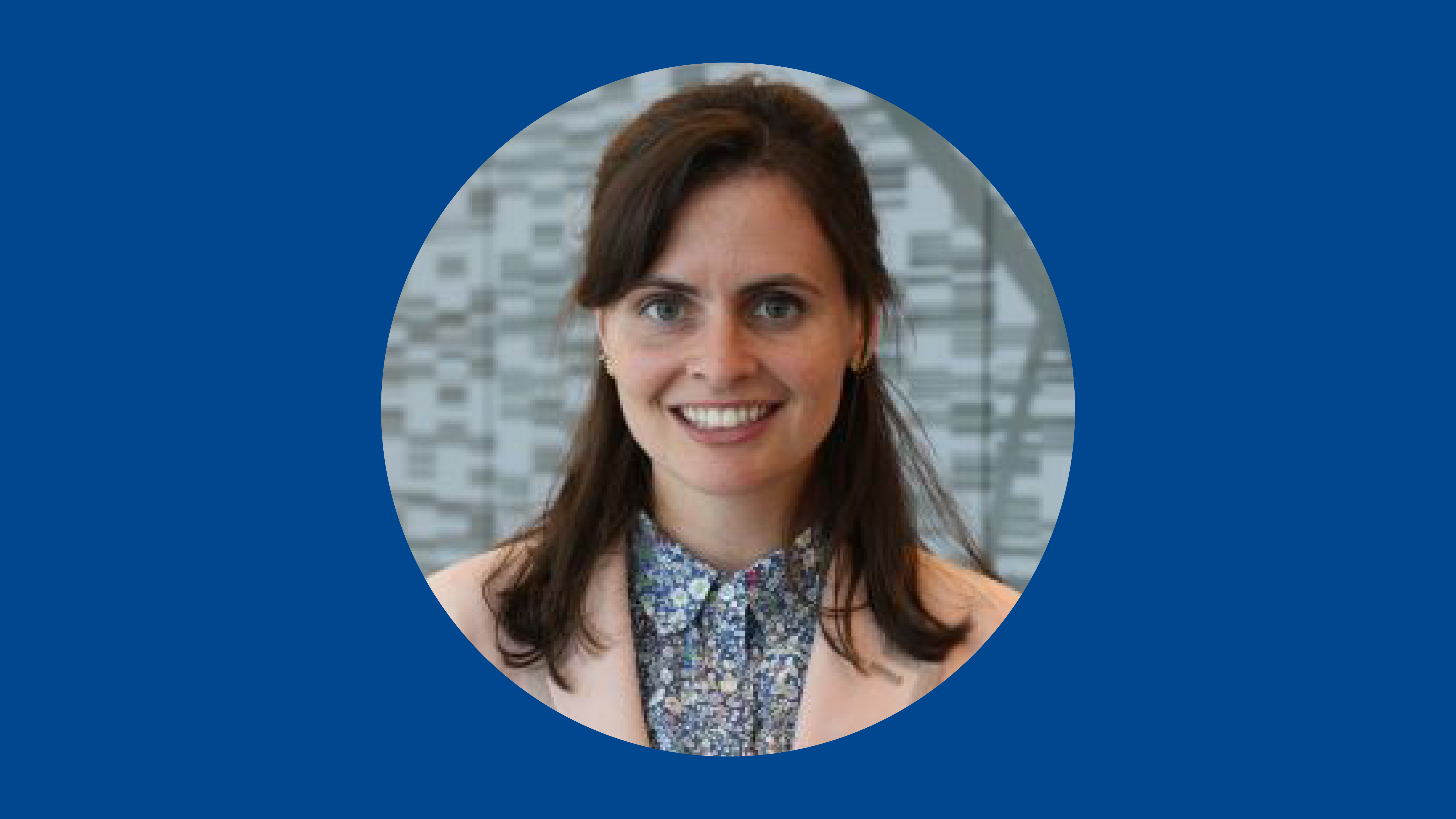 Photo of woman with brown hair wearing pink blazer on on blue background.