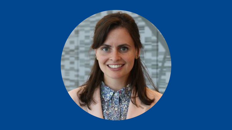 Photo of woman with brown hair wearing pink blazer on on blue background.
