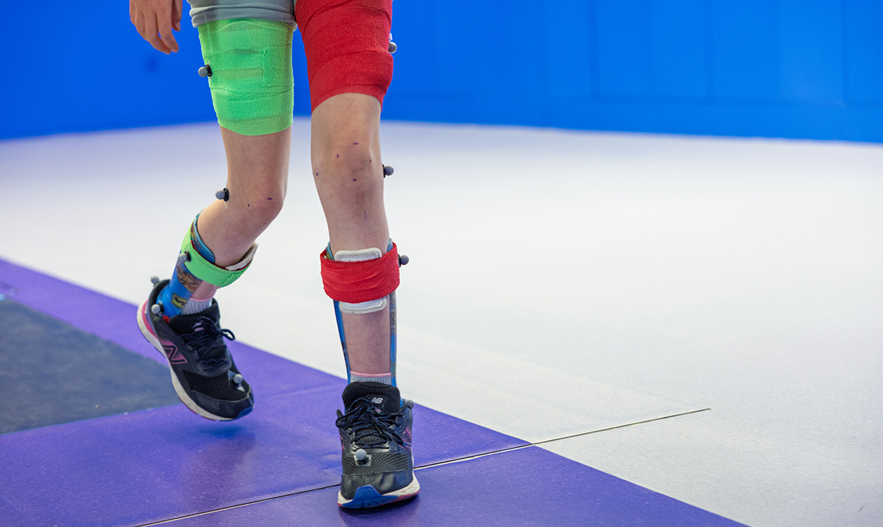 Close-up of an athlete's lower legs and feet, wearing sportswear, ankle supports and sneakers, stepping on a blue sports mat.