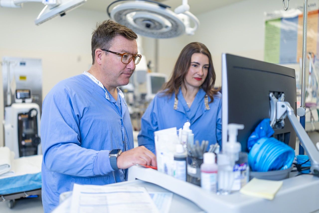 A man and a woman in scrubs look at a screen together in an operating room.