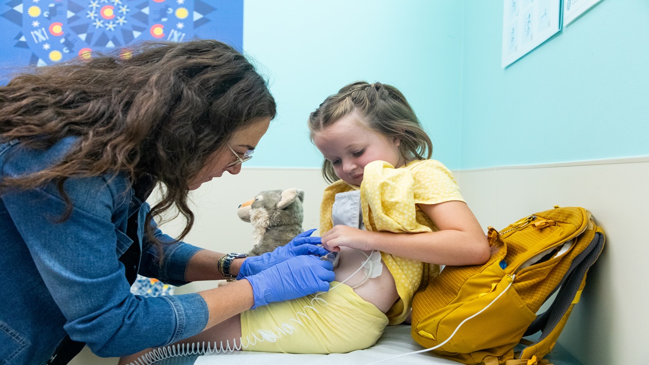 Woman with gloves puts device on the belly of a child in a yellow outfit