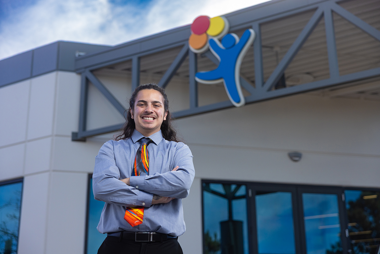Xavier Archuleta, a Patient Registration Representative standing smiling with arms crossed in front of Children's Hospital Colorado building 
