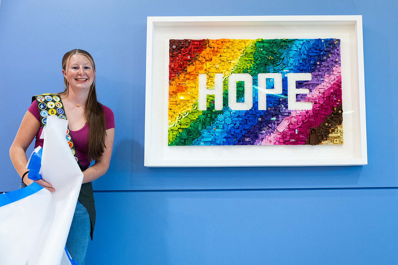 Former patient Makenna standing next to colorful mural with the word "Hope" across it 
