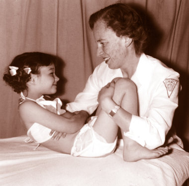 An old photo of a woman in white holds a young girl while bending her legs