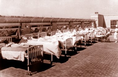 An old photo of 9 hospital beds lined up on the roof so the patients in them can get some sun