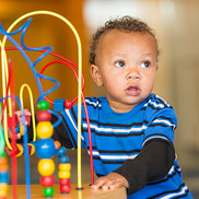 A toddler wearing a blue striped shirt plays with a wooden maze toy.