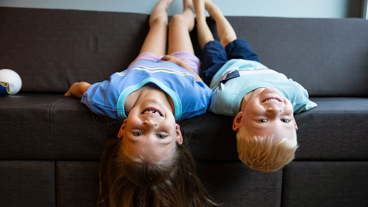 Two children hanging upside down off a couch and smiling