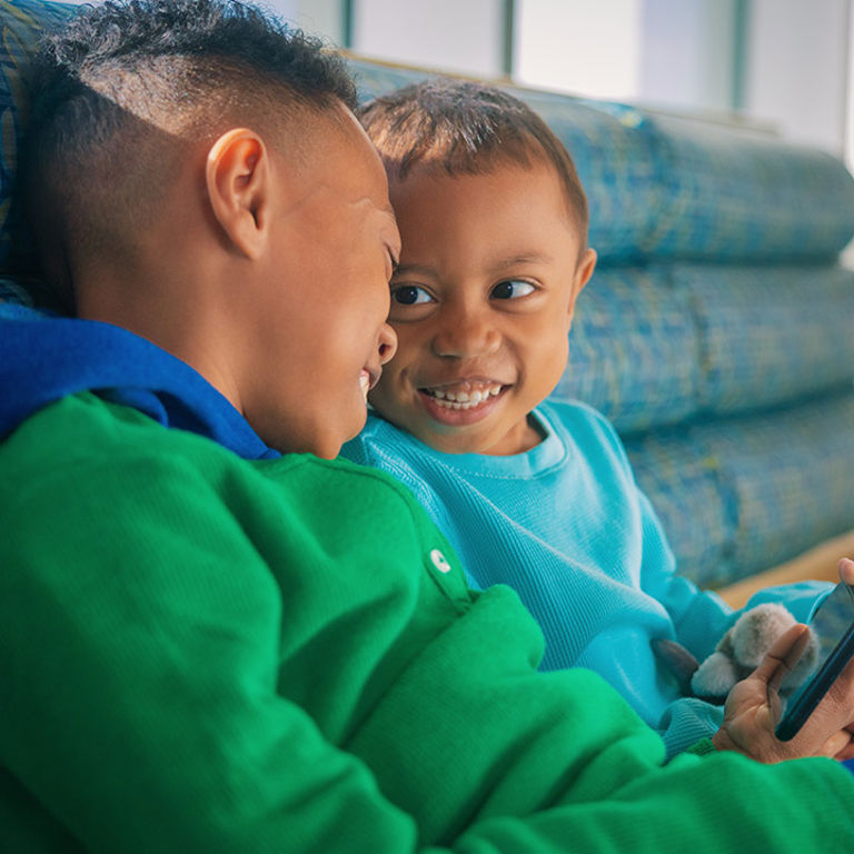 Two boys laugh and look at a cell phone screen together