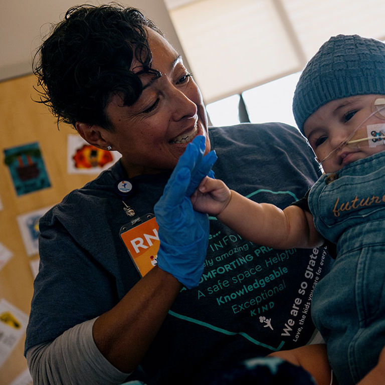 Nurse smiles at an infant who has NG and oxygen tubes