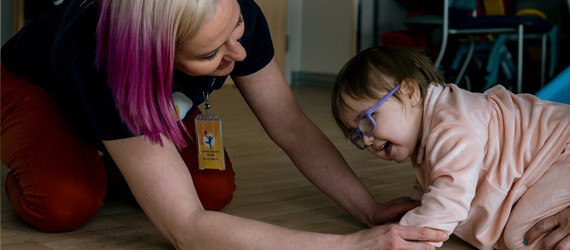 A physical therapist helps a baby get in the crawling position