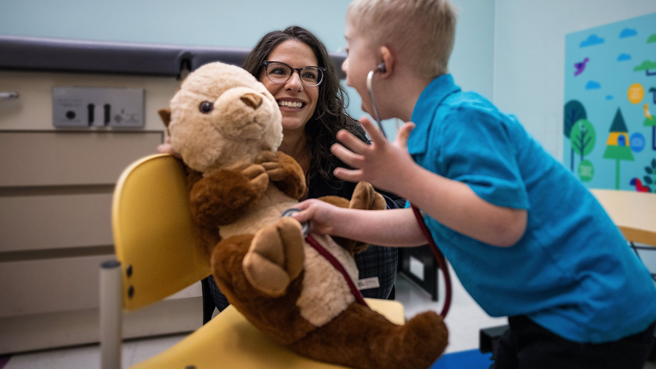 Young boy pretends to use a stethoscope on a stuffed otter