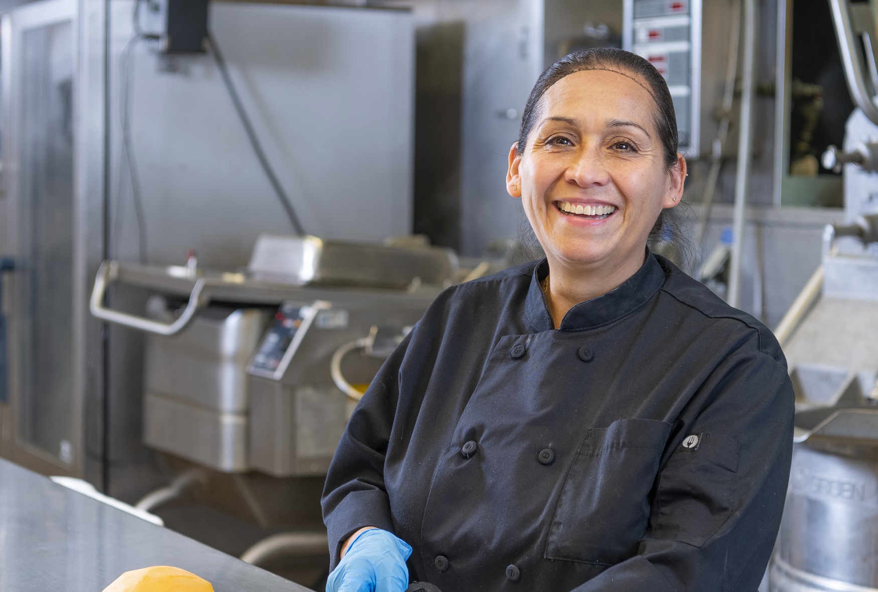 Woman chopping squash in a commercial kitchen and smiling.