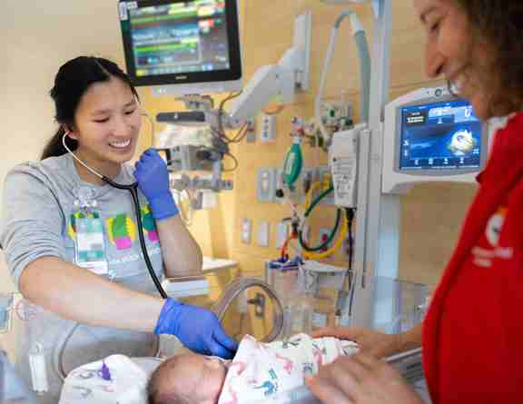 Clinicians examining a baby in a hospital bed with a stethoscope  