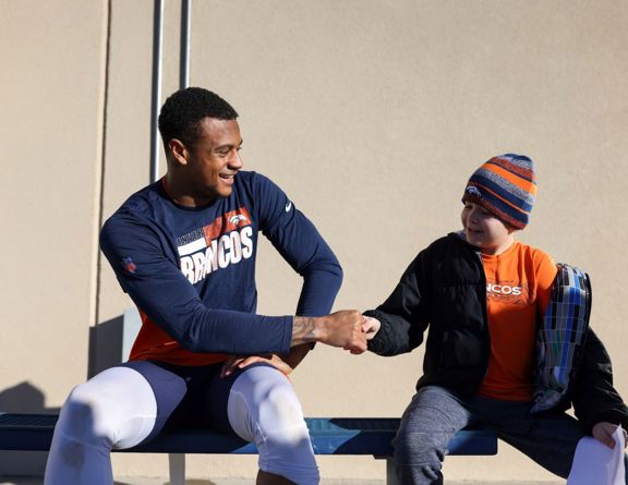 Denver Broncos football player shaking hands with a child. 