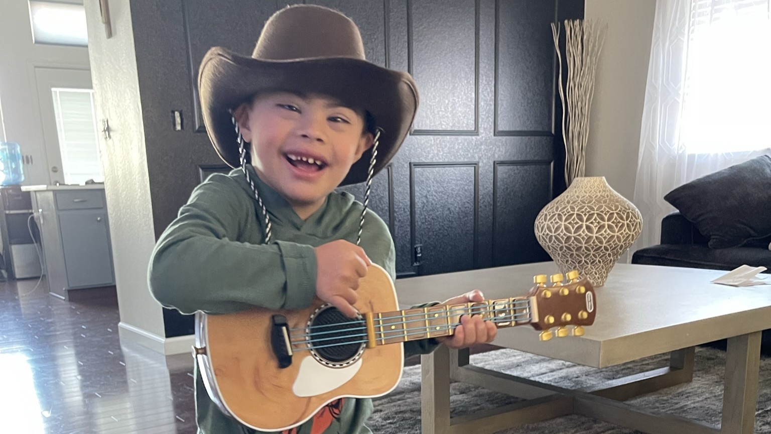 A young boy plays a guitar while wearing a cowboy hat.