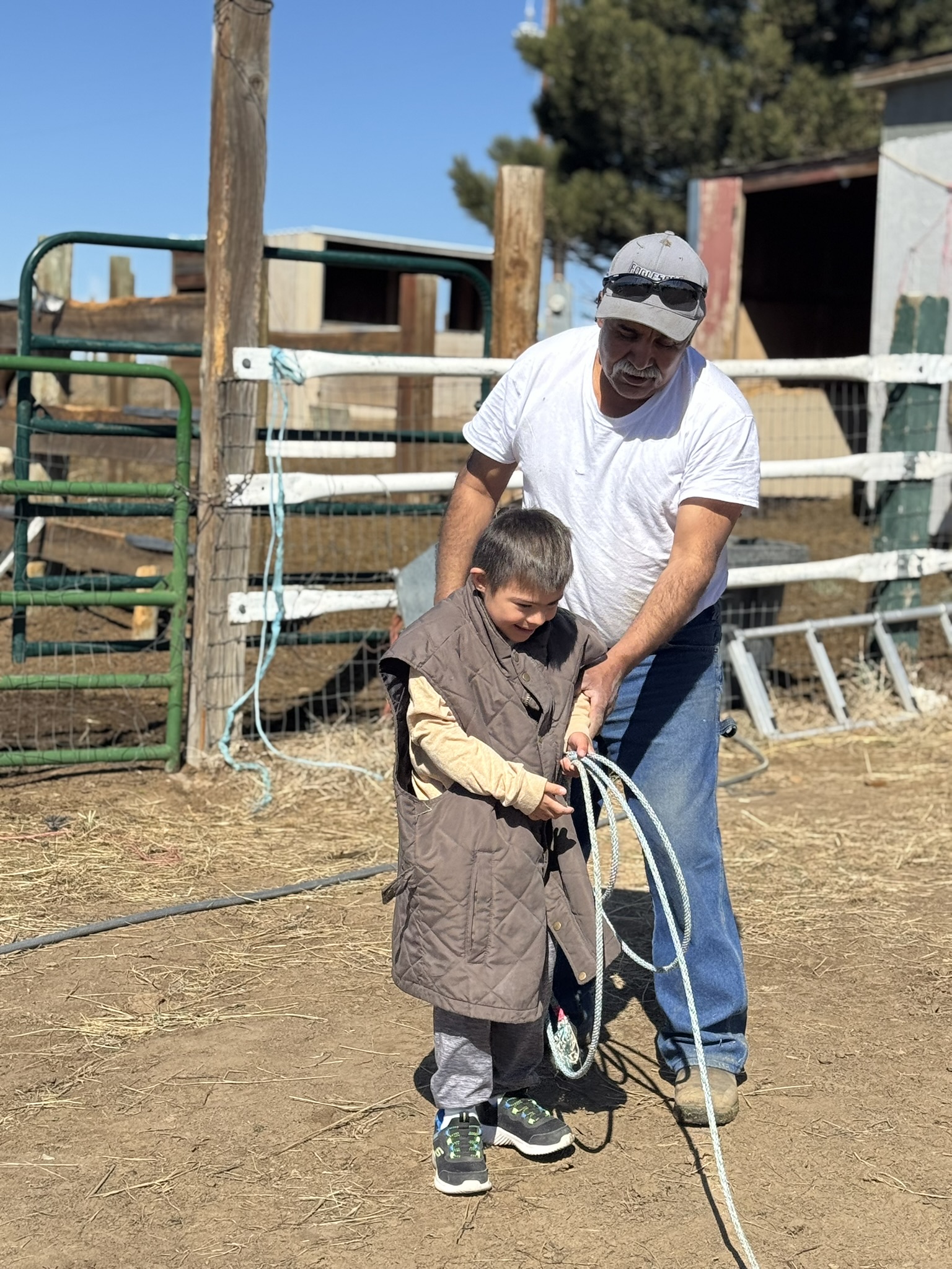 A child wears a vest and holds a rope at a ranch taking care of horses. 