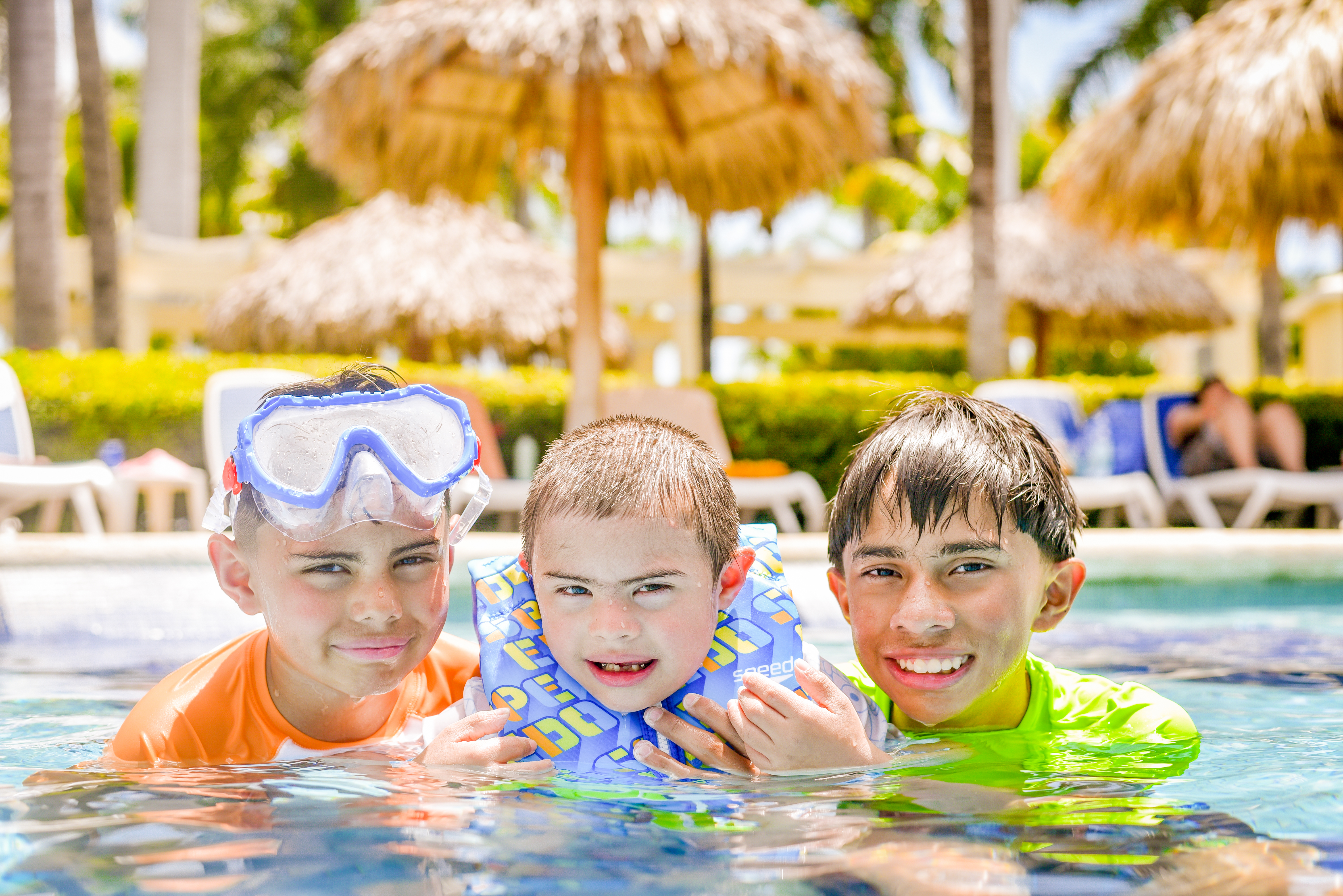 Three young boys swim in a pool with floaties and swim goggles.  