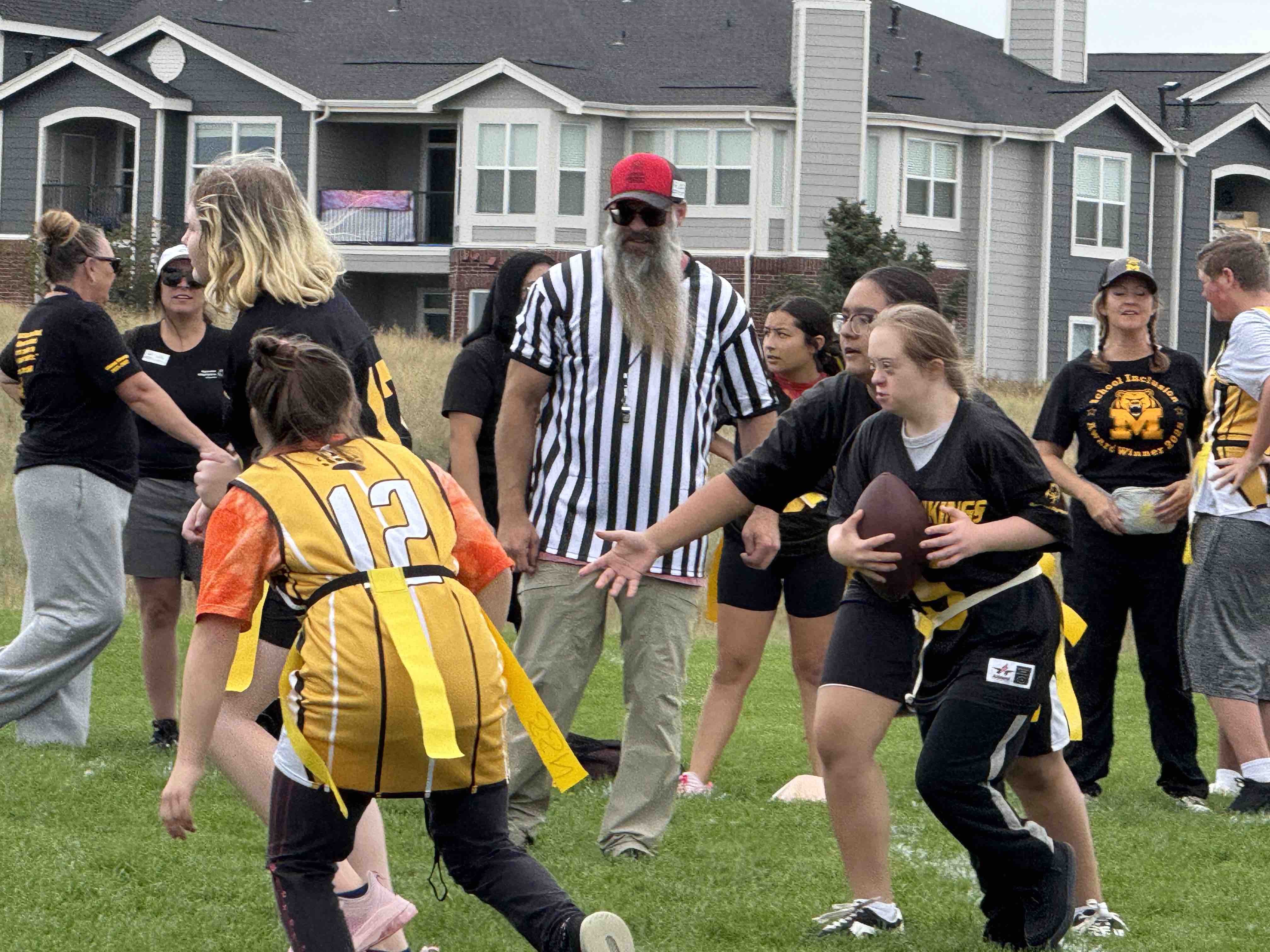 A group of children play flag football with a referee in the back.