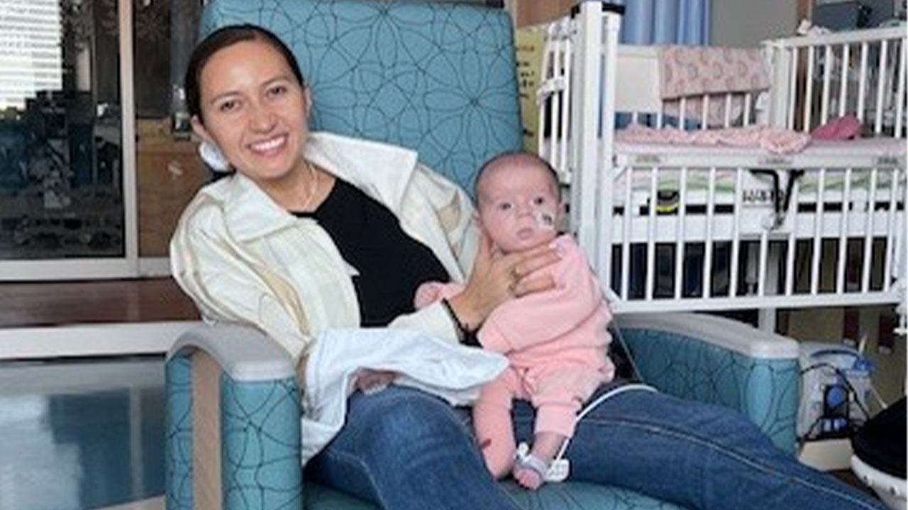 A parent smiles and holds their newborn baby in a hospital chair.