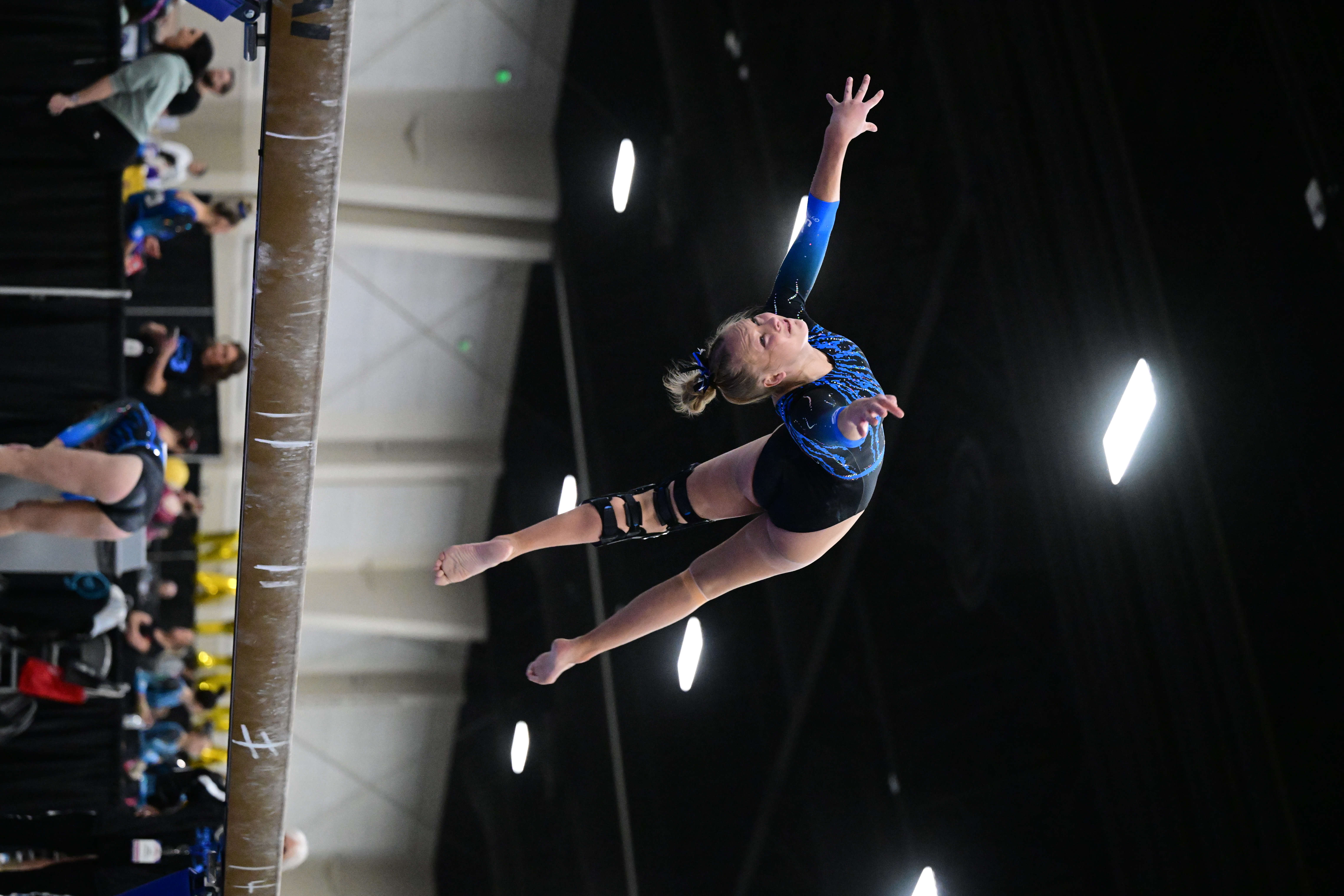 Gymnast in blue leotard flipping upside down over the balance beam. 