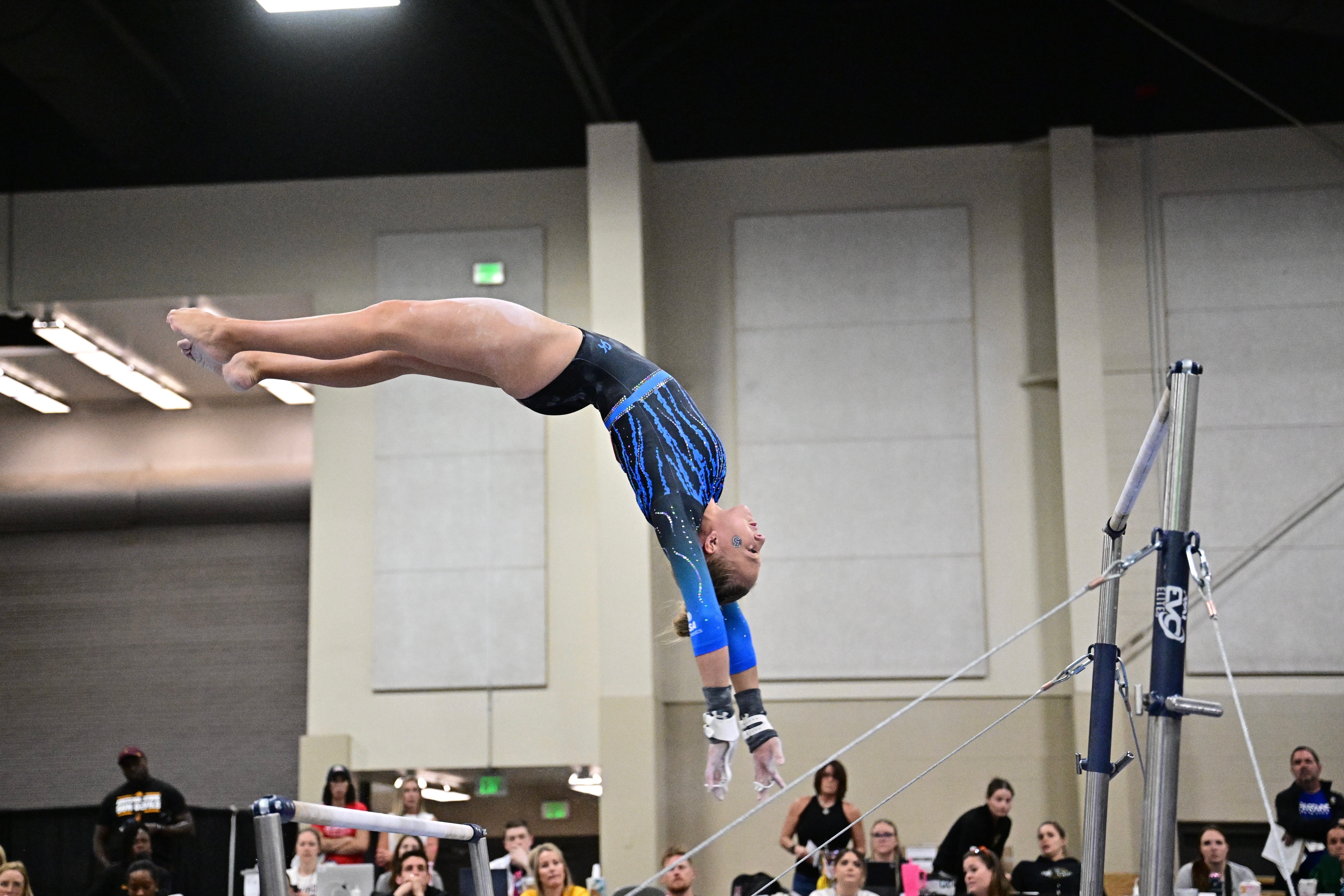 Gymnast in blue leotard flipping upside down by the uneven bars in a gym