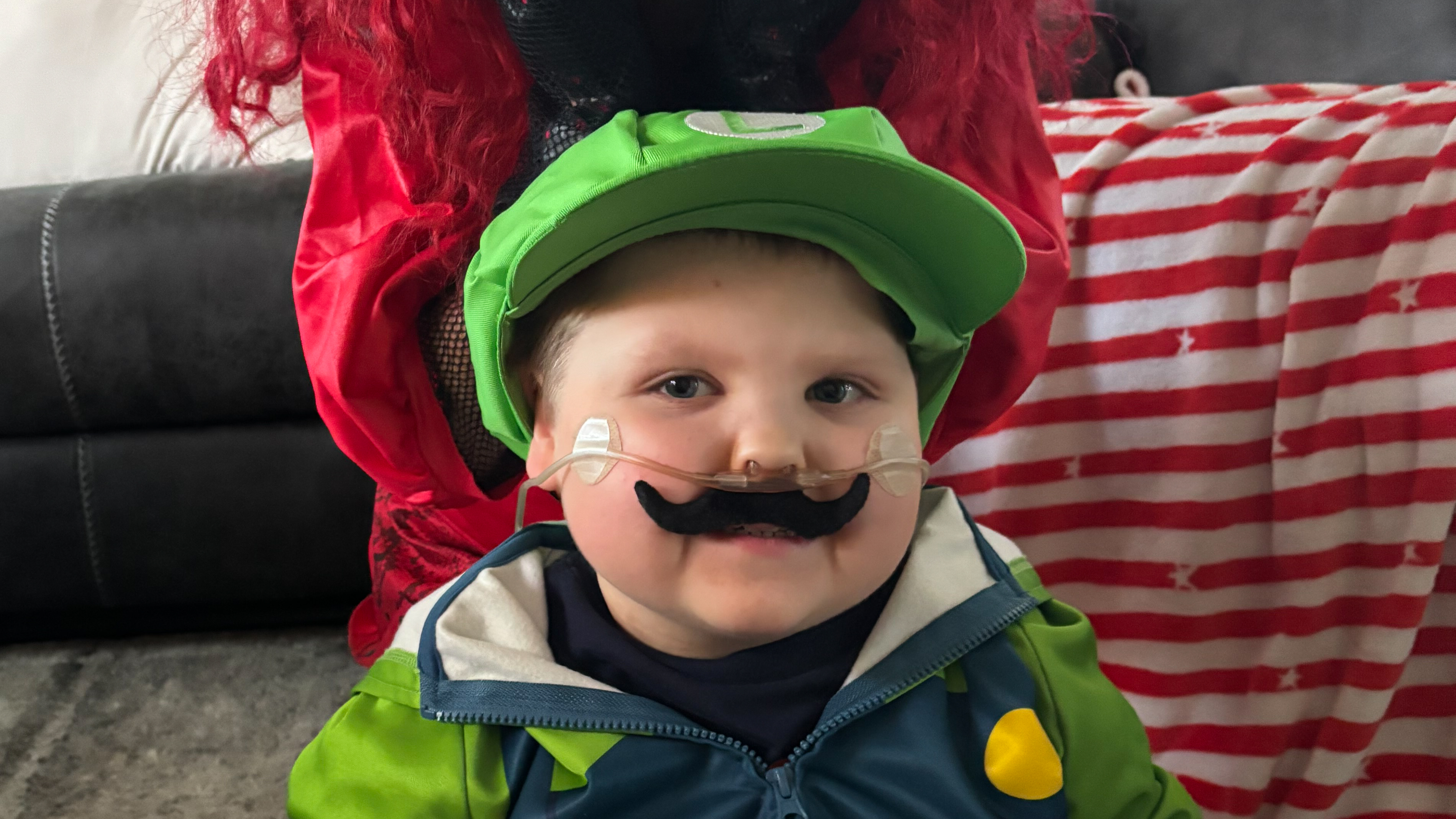 Conor is dressed up as Luigi from the Mario and Luigi video game. He is wearing a green costume with a matching cap and a blue jacket featuring yellow accents. 