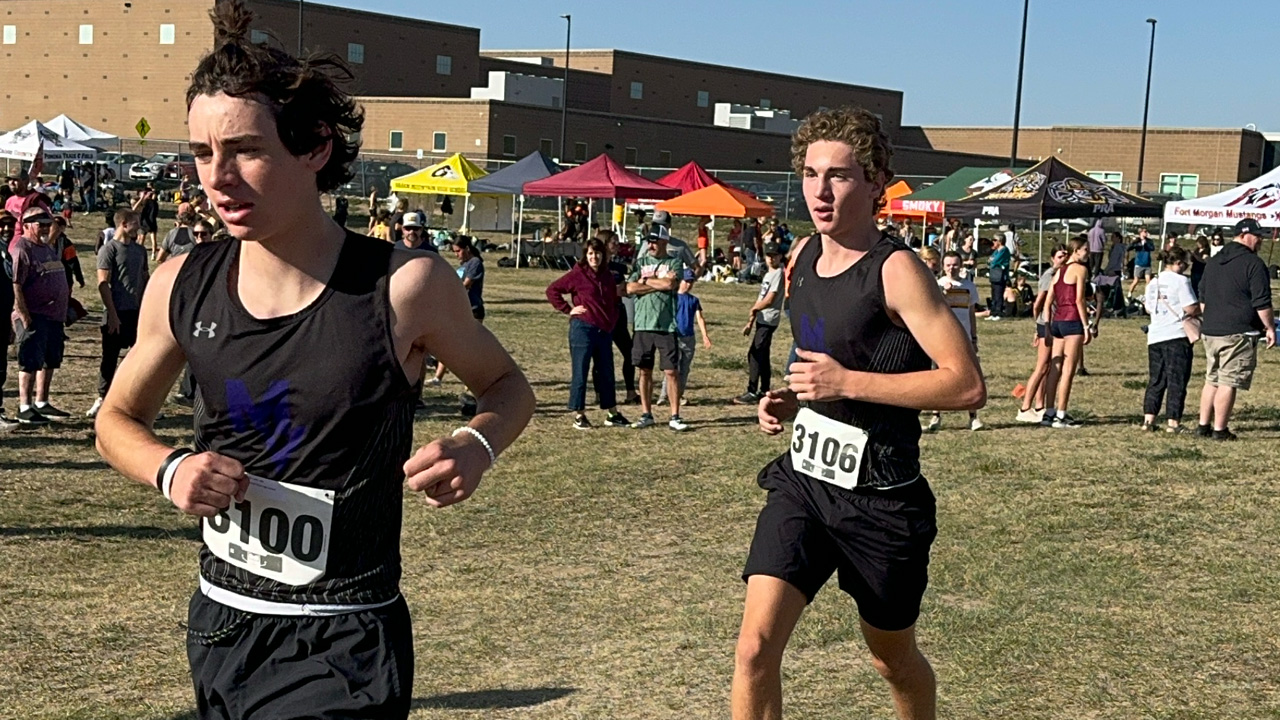 A person running on grass, wearing black shorts and a black tank top with numbers on the front.