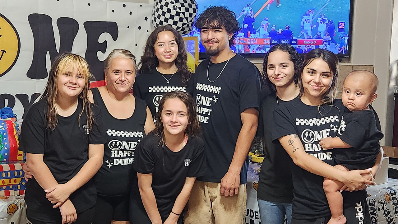 Jaycee and several members of her family smile together at a birthday party and several people wear matching shirts themed for the party.