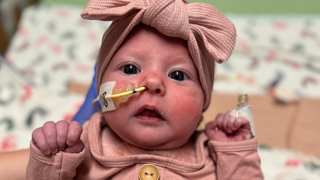 Close up of baby wearing a bow in the NICU staring at the camera with a tube coming out of their nose