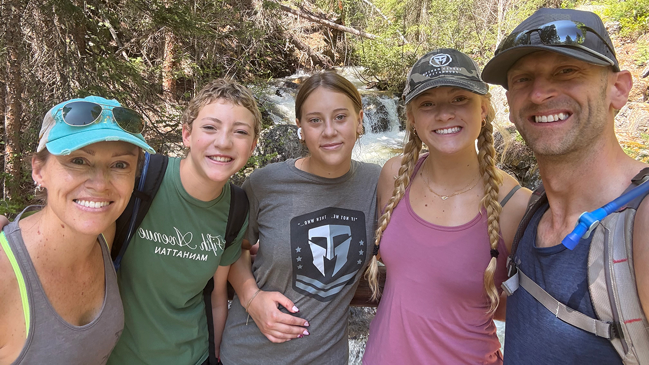 Five people pose for a photo on a forest hiking trail with a stream and waterfall in the background.