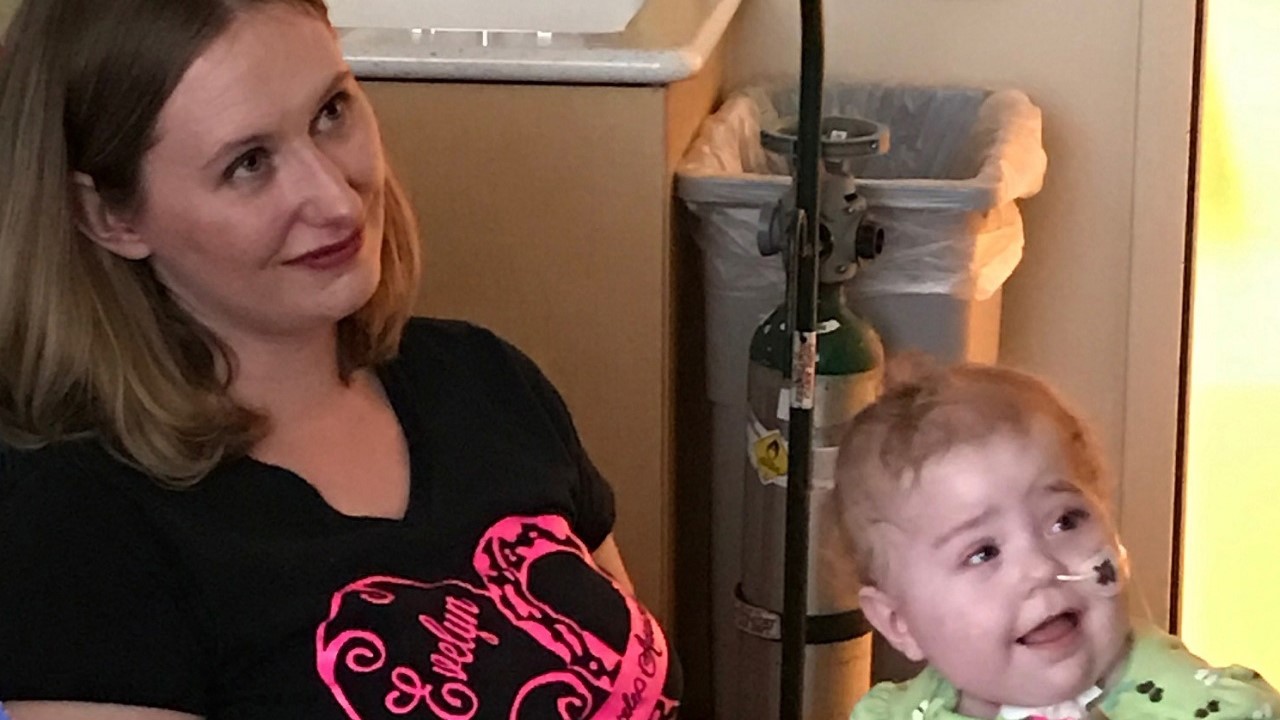 Evelyn sits with her mom in a hospital exam room while both smile.