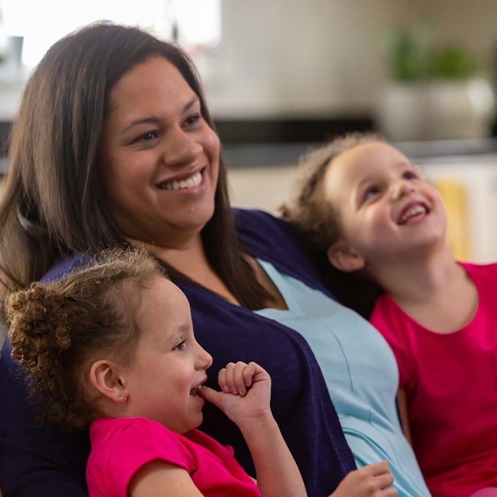 A mom sits between her twin daughters, who overcame TTTS. All three are smiling widely.