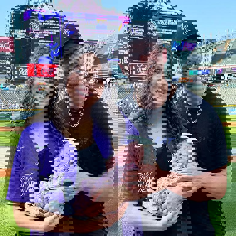 A couple smiles holding their young infant at a Rockies game