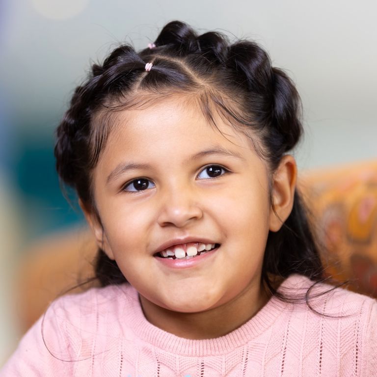 Girl with black hair wearing a pink sweater smiling