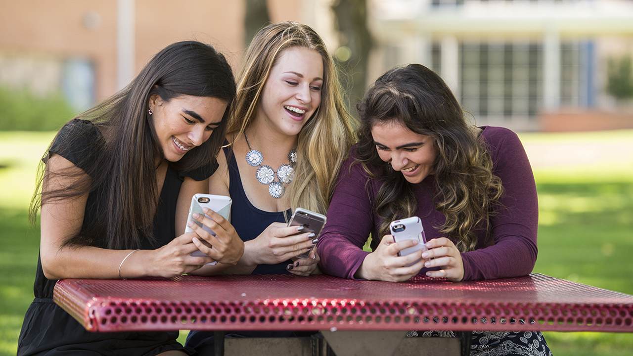 Three teenage girls laugh with their phones