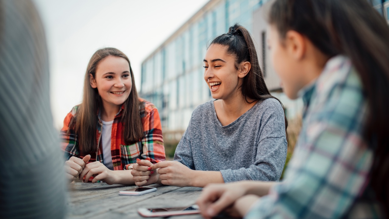 Three teenage girls laugh with their phones