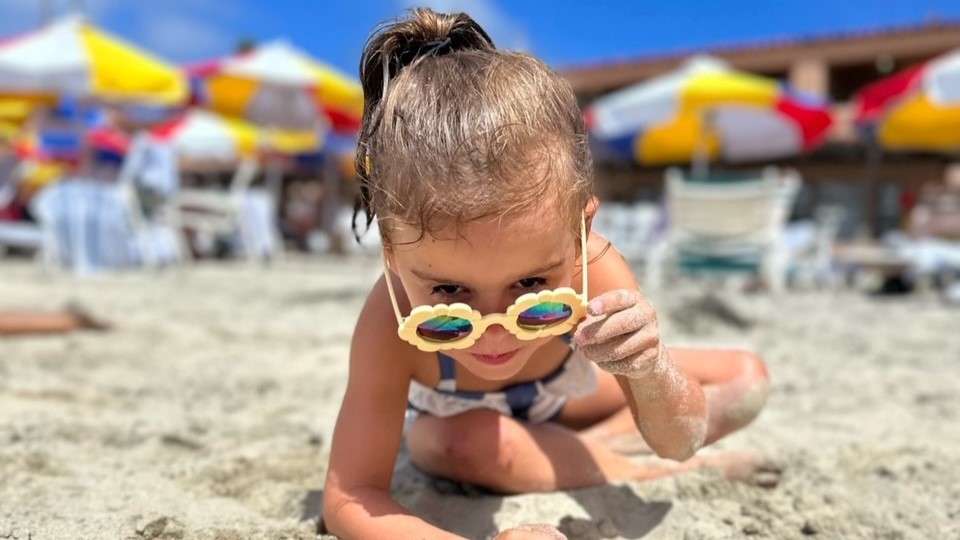 Emma on the beach pulls yellow, flower sunglasses down her nose.