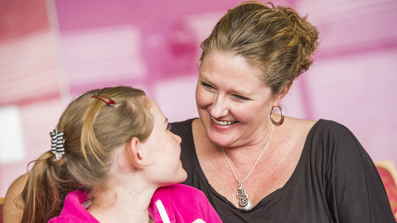 Neuroscience Family Resources A close-up of a woman in a black shirt and a girl in a pink sweatshirt smiling at each other.