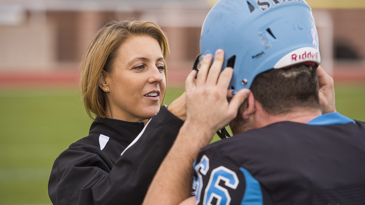 Athletic trainer helps football player adjust helmet.